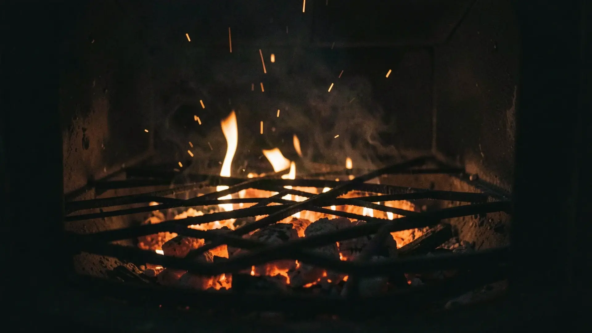 Glowing embers and low flames under a black iron grill